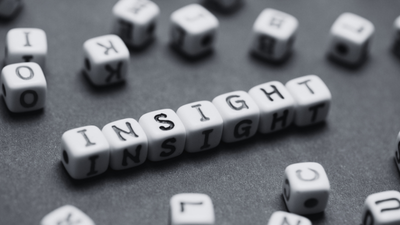 White letter cubes spell INSIGHT on a gray surface, symbolizing insight. Unsure context clarified by surrounding blocks.