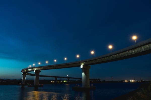 Nighttime view of a curved bridge lit by streetlights spanning over a calm river.
