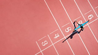 Athlete in a blue shirt sprinting on a red track with white lane lines marked 3–6.